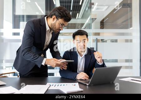 Two professionals collaborate in modern office using laptop and smartphone, emphasizing teamwork, technology, productivity. Engaged managers discussing ideas, showcasing business strategy Stock Photo