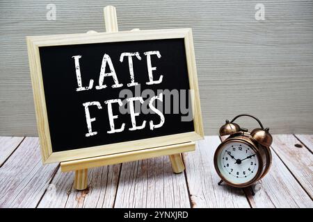 Late Fees text written on chalkboard with alarm clock on wooden background Stock Photo