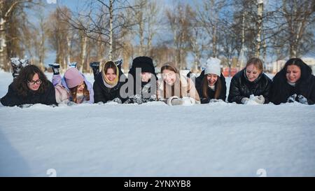 Young female students having fun together on a snowy winter break, smiling and lying on a blanket of fresh snow Stock Photo