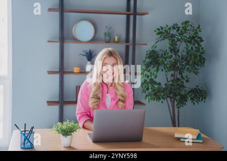 Young woman enjoying leisure time at home, working remotely on laptop in cozy living room with natural lighting and plants Stock Photo