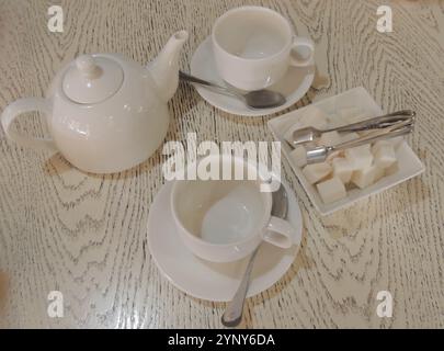 white ceramic tea set on light textured wooden tabletop, two mugs, teapot and sugar bowl as still life for tea party Stock Photo