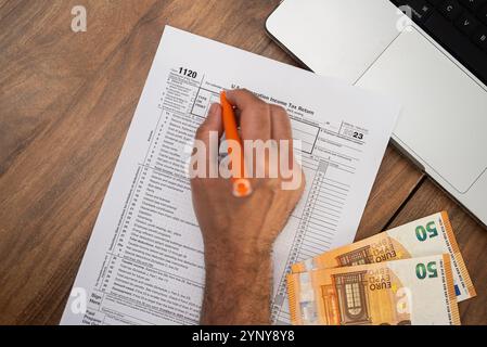 Filling out U.S. corporation income tax return form 1120 with euros on a wooden desk. Tax season, accounting, and financial planning concept. Stock Photo