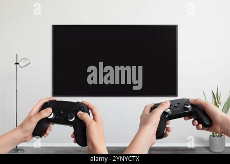 Two players holding gamepad in front of a TV with a blank screen, designed for video game promotion and mockup presentations Stock Photo