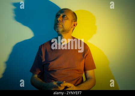 White man leaning against a wall with blue and yellow colored lights above him. Studio portrait. Flash art. Stock Photo