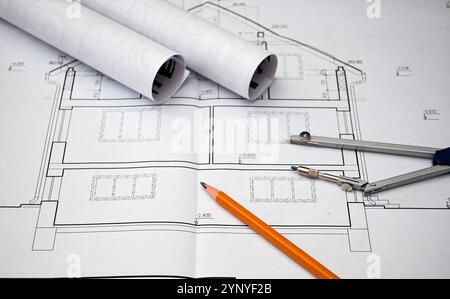 Architectural project with compass, pencil and rolled blueprints lying on construction plans of a house. Stock Photo