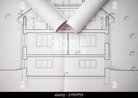 Rolled blueprints are lying on top of unfolded house plans, showcasing precise measurements and architectural details. Stock Photo