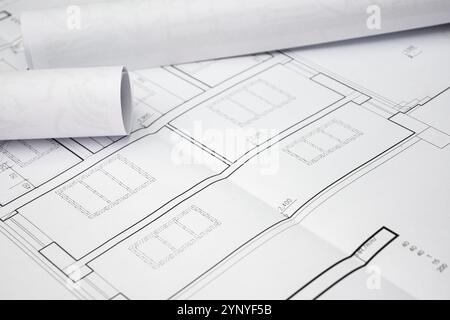Rolled blueprints are lying on top of unfolded house plans, showcasing precise measurements and architectural details. Stock Photo