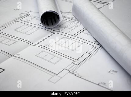 Rolled blueprints are lying on top of unfolded house plans, showcasing precise measurements and architectural details. Stock Photo