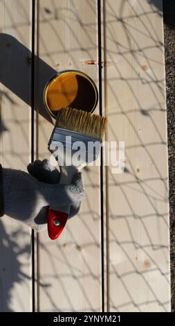 hand in glove holding brush over paint or varnish can over textured light boards top view Stock Photo
