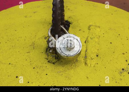 Close-up of white painted locked combination padlock attached to rusted steel handle on yellow painted concrete bell shaped block, Quebec, Canada, Nor Stock Photo