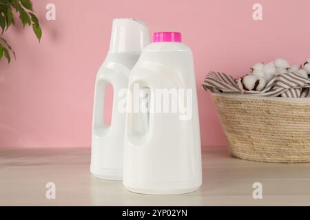 Bottles with laundry detergent and clothes in basket on wooden table against pink background Stock Photo