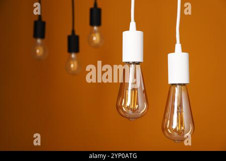 Light bulbs hanging on cords against orange background Stock Photo