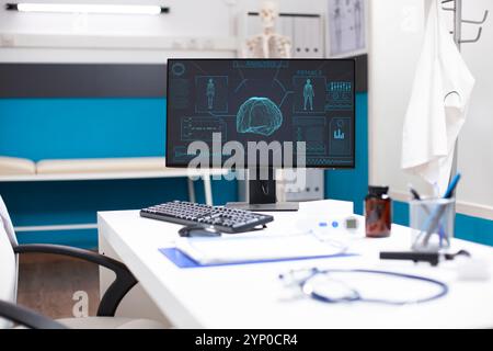Modern desk in medical office holds a computer showing hud imaging of body and brain, emphasizing cutting-edge diagnostic technology. Nobody in clinic room, allowing focus on equipment and analysis. Stock Photo