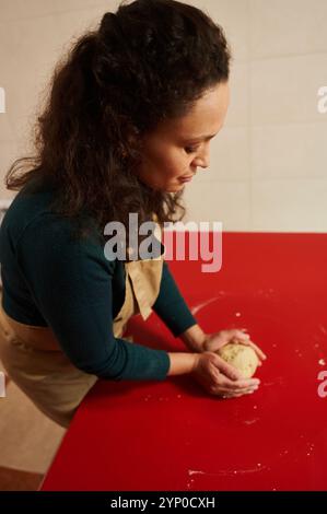 Focused woman kneads dough on a vibrant red countertop in a warm kitchen setting. The image captures the essence of homemade cooking and the joy of ba Stock Photo