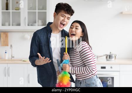 Funny asian couple singing songs while cleaning kitchen Stock Photo