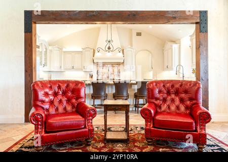 Cozy living area with elegant red chairs and a spacious kitchen in view Stock Photo