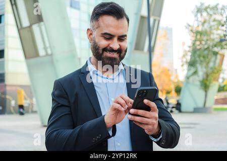 Confident mature businessman using a cellphone outdoors in a modern cityscape, wearing formal suit, smiling and staying productive, showcasing professional success, communication, and connectivity. High quality photo Stock Photo