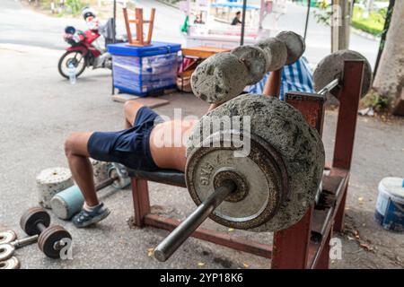 Old homemade barbell and dumbbells made of concrete bucket on the ground. a man lifts a homemade dumbbells in an outdoor gym. The concept of sports fo Stock Photo