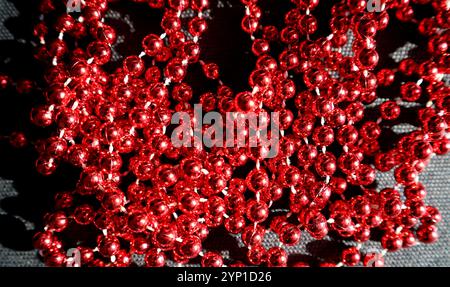 Red shiny beads are randomly placed on a black background. Macro photo. Garland. The beads are connected by a white thread. Thrown on top of each othe Stock Photo