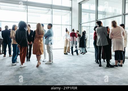 A group of people networking and engaging in discussions at a business conference event. Diverse crowd engaging in casual conversations in a modern co Stock Photo