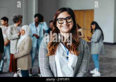 Successful businesswoman smiling confidently at a corporate networking event with diverse colleagues in a contemporary office environment. Stock Photo