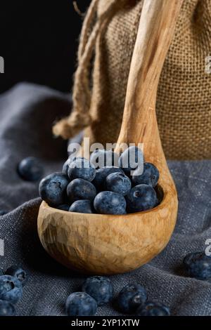 Hand sculpted wooden ladle filled with fresh blueberries on a gray kitchen cloth Stock Photo