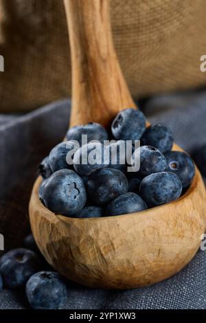 Hand sculpted wooden ladle filled with fresh blueberries on a gray kitchen cloth Stock Photo