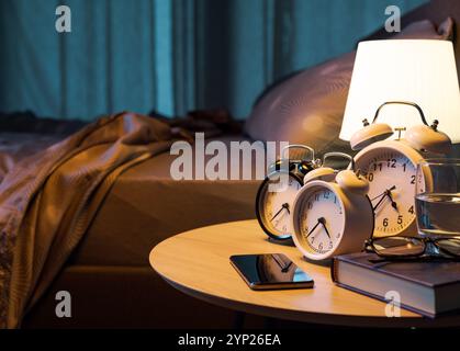 Many alarm clocks and smartphone on the bedside table in the bedroom, deadlines and reminders concept Stock Photo