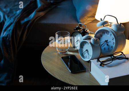 Many alarm clocks and smartphone on the bedside table in the bedroom, deadlines and reminders concept Stock Photo