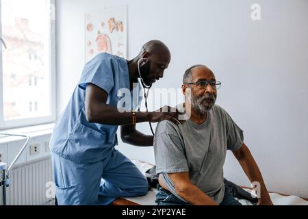 Male medical professional checking senior man's back with stethoscope in examination room at clinic Stock Photo