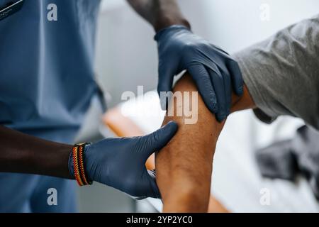 Male doctor wearing surgical glove checking hand of patient in clinic Stock Photo
