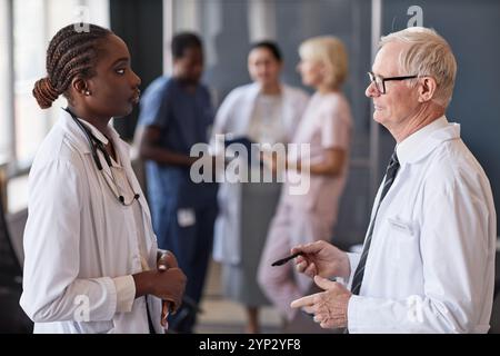 Side view of young African American female doctor in conversation with senior chief physician listening to expert opinion at training seminar at medic Stock Photo
