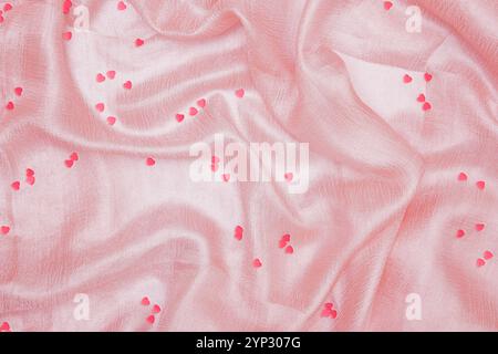 Small pink hearts lying on a light pink silk fabric Stock Photo