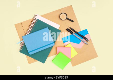 Office and school supply on a light yellow background. Notebooks, pen, pencil, envelopes, stickers, magnifier. Top view. Stock Photo