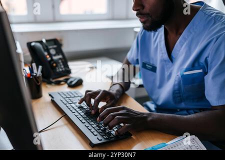 Male doctor working on computer while sitting in examination room at clinic Stock Photo