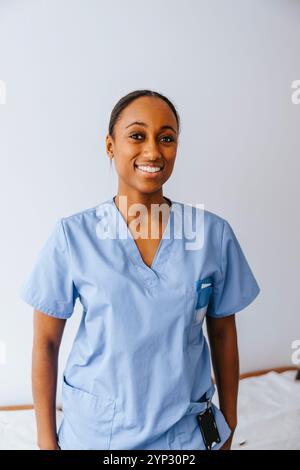 Portrait of female medical professional in blue scrubs standing in front of white wall at clinic Stock Photo