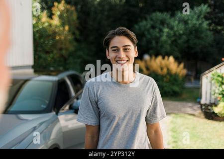 Happy young man wearing gray t-shirt standing in back yard Stock Photo