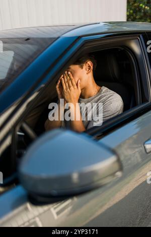 Tired young man covering face with hands sitting in car Stock Photo