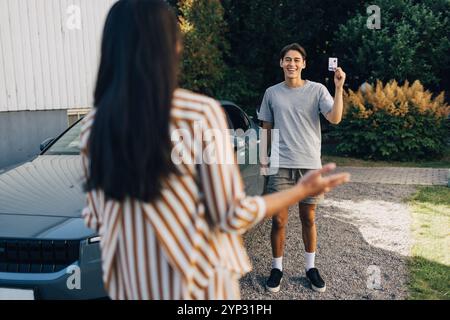 Happy young man showing drivers license to mother standing in back yard Stock Photo