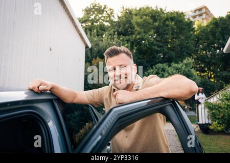 Portrait of smiling mature man leaning on car door in back yard Stock Photo