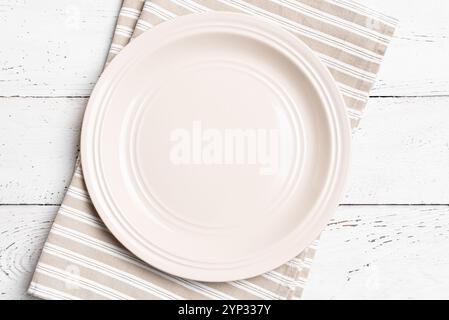 Empty beige plate with rustic linen napkin on white wooden table, top view, space for meal design. Food template background, catering mock up. Stock Photo