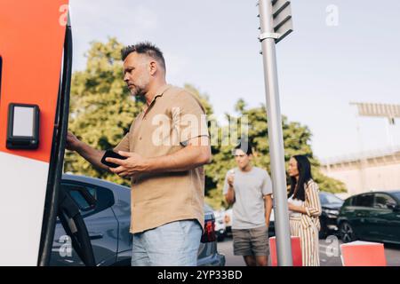 Low angle view of mature man doing mobile payment at electric vehicle charging station Stock Photo