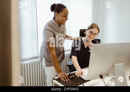 Smiling female doctor with hand on shoulder of nurse using computer at hospital Stock Photo
