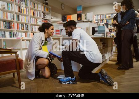 Smiling man and woman glancing at each other while picking up books at shop Stock Photo
