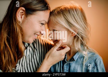 Smiling mother touching chin of son with long blond hair at home Stock Photo
