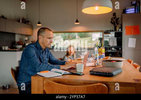 Focused businessman working on laptop while sitting near dining table at home Stock Photo