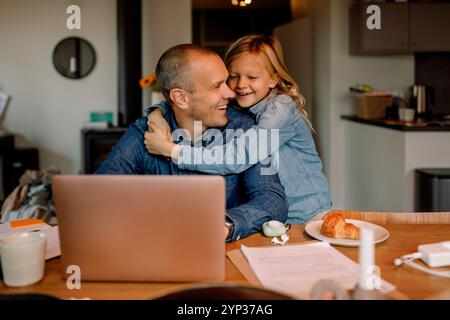 Happy boy embracing father working on laptop at home Stock Photo