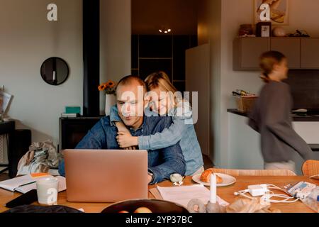 Smiling boy with arm around father working on laptop at home Stock Photo