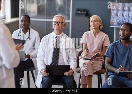Senior male head physician listening to colleagues presentation with diverse team of doctors while participating in seminar at conference room Stock Photo