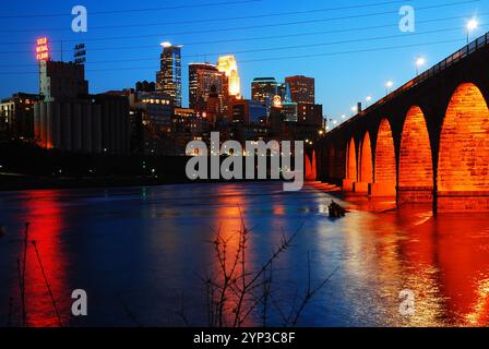 The skyline of Minneapolis, Minnesota and the Stone Arch Bridge are reflected in the water of the Mississippi River at sunset Stock Photo